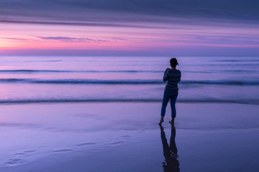 A woman standing quietly at the edge of the sea at dusk